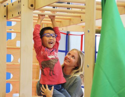 An occupational therapist smiling with a boy as he climbs a wooden climbing frame