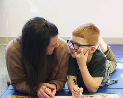 An occupational therapist lying on the floor playing alongside a smiling boy