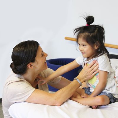 A therapist sitting on a therapy mat with a smiling toddler